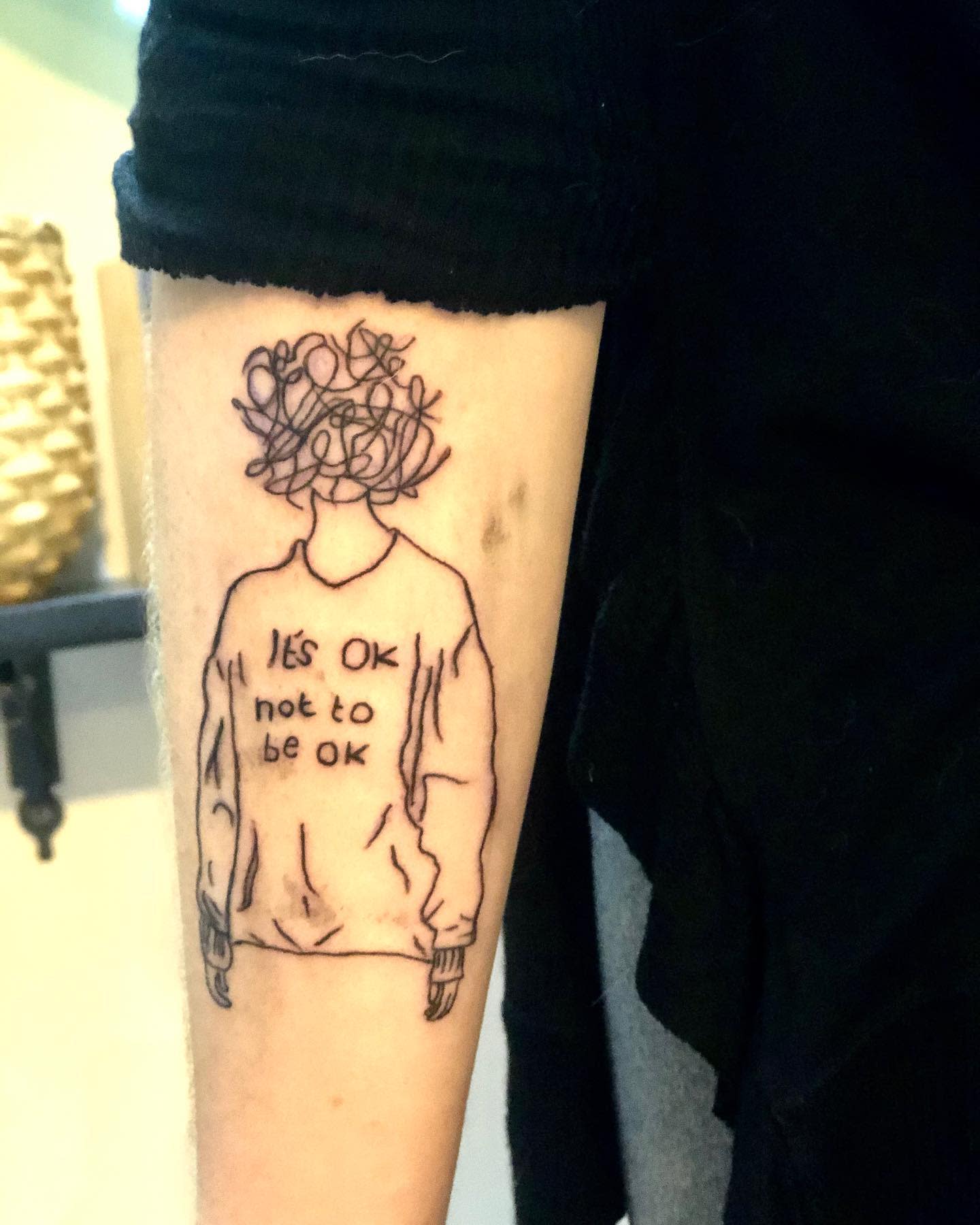 Tattoo of a figure with a scribbled head and a shirt that reads "It's OK not to be OK"